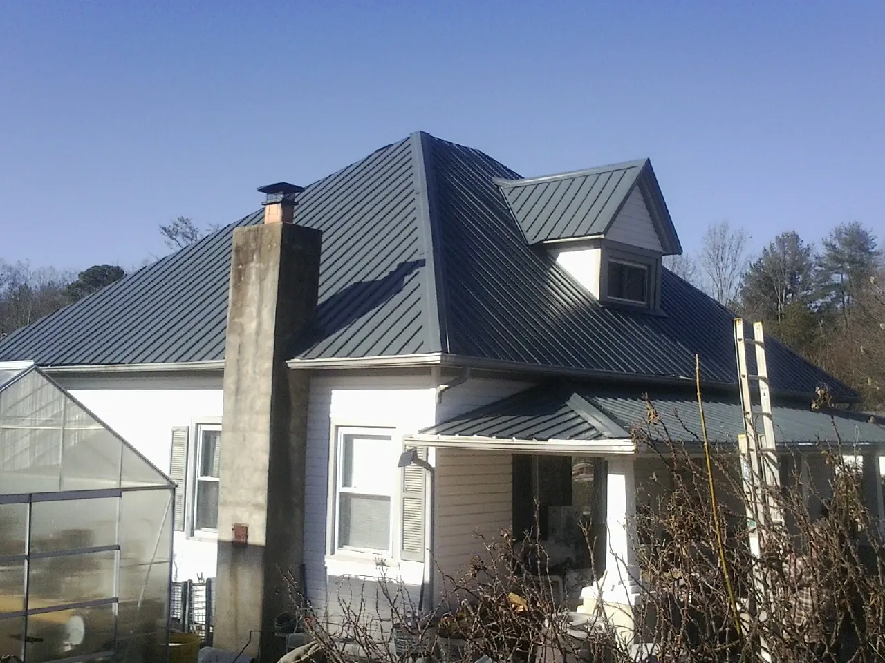 Dark blue standing seam metal roof on a white farmhouse with dormer — Slate & Tile Roof Repair by Roofing Brothers in Clemmons