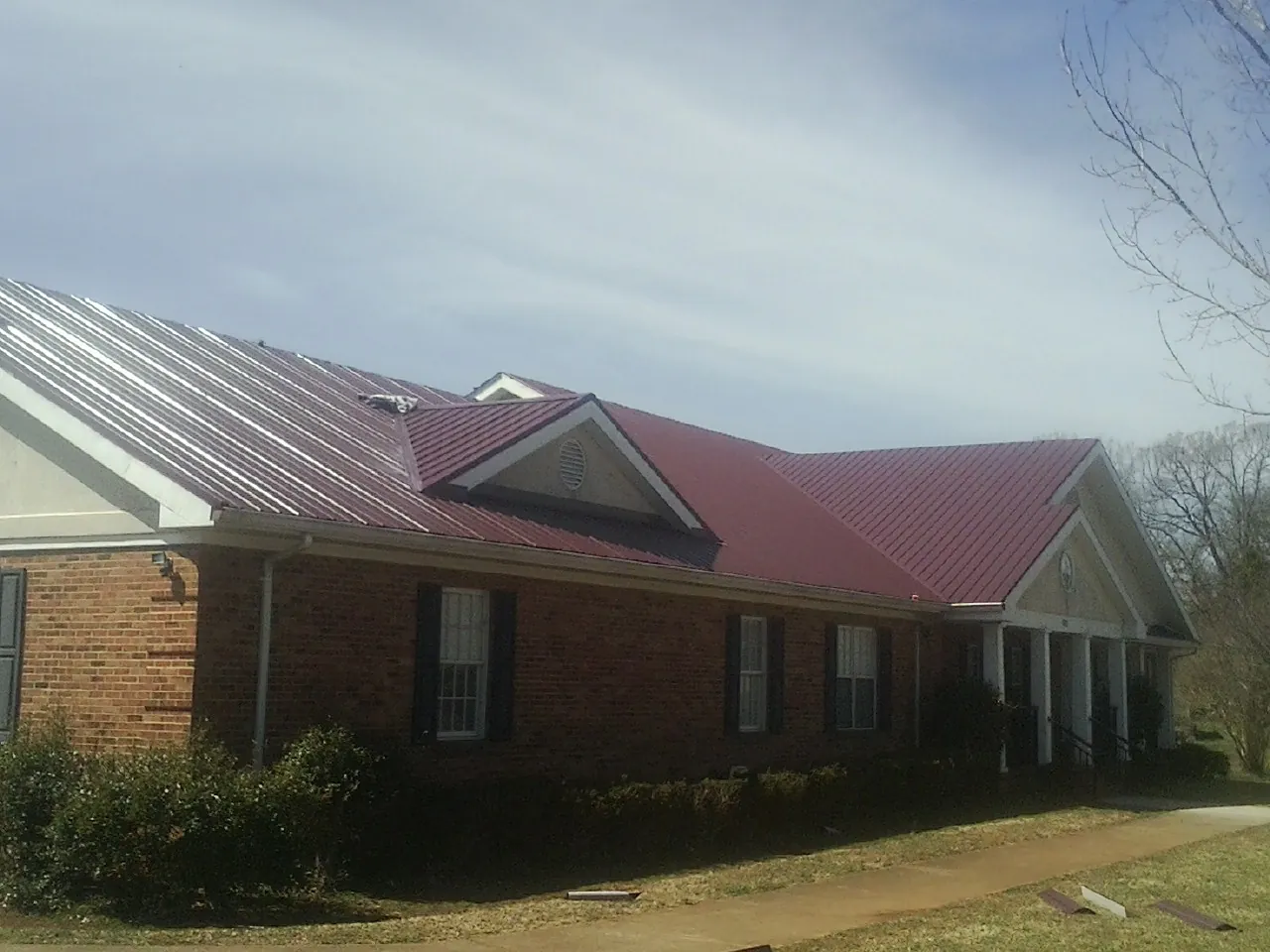 Red metal roof with gabled entries on a long brick building, from a Hail Damage Roof Repair job in Clemmons