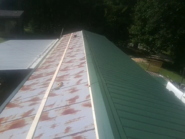 Old rusted panels beside newly installed green metal roofing — Wind Damage Roof Repair by Roofing Brothers in Clemmons