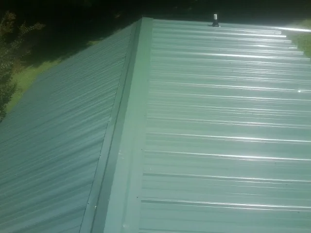New green metal panels meeting at the ridge of a roof — Flat Roof Repair work by our crew in Clemmons