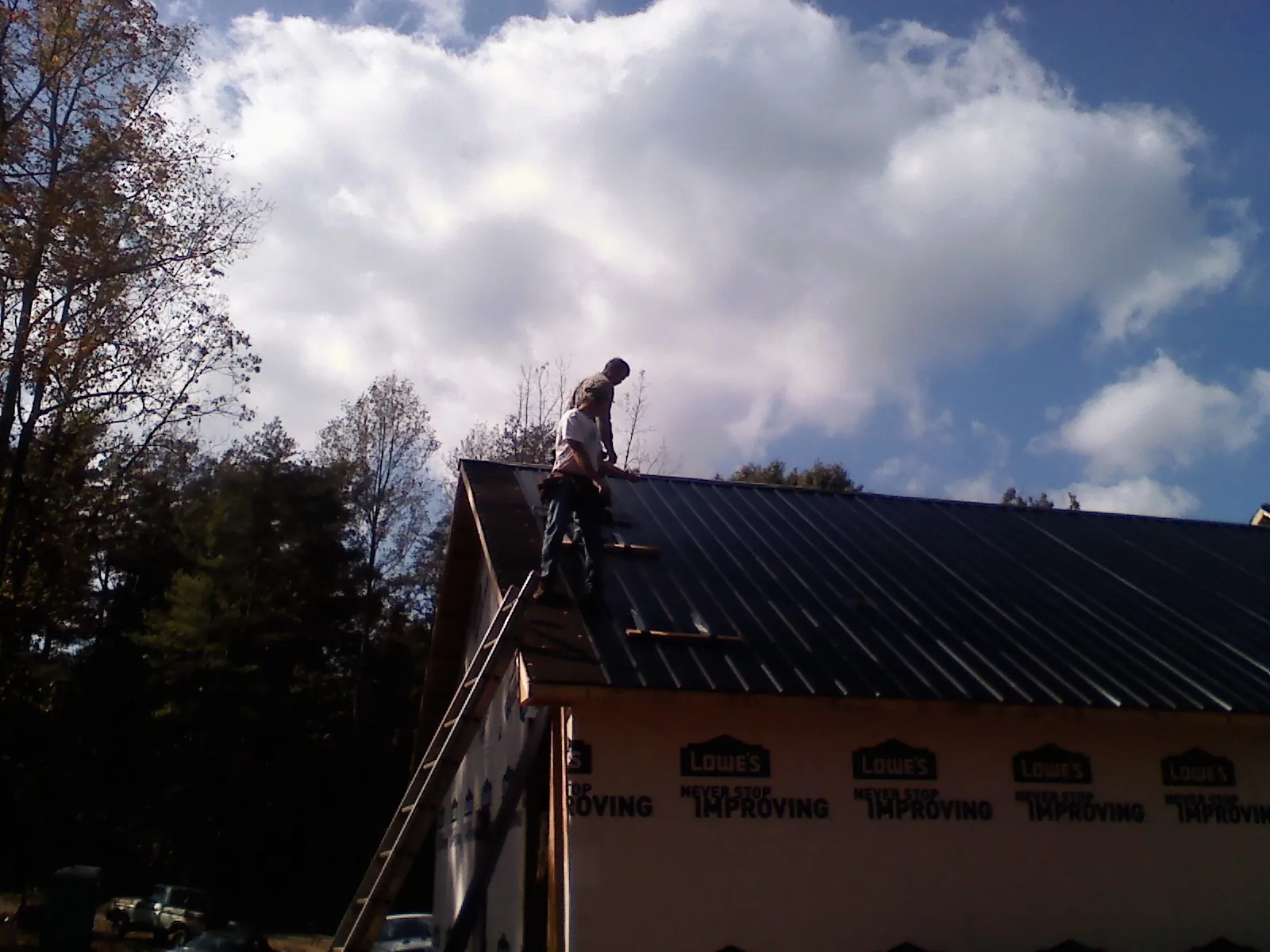 Roofer fastening dark metal panels high against a cloudy sky, from a Roof Inspection job in Clemmons