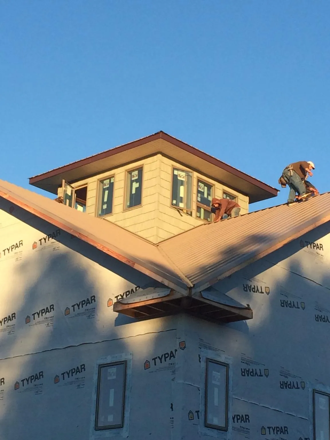 Roofers working around a rooftop cupola on a new metal roof at sunset — Roof Waterproofing in Clemmons by Roofing Brothers